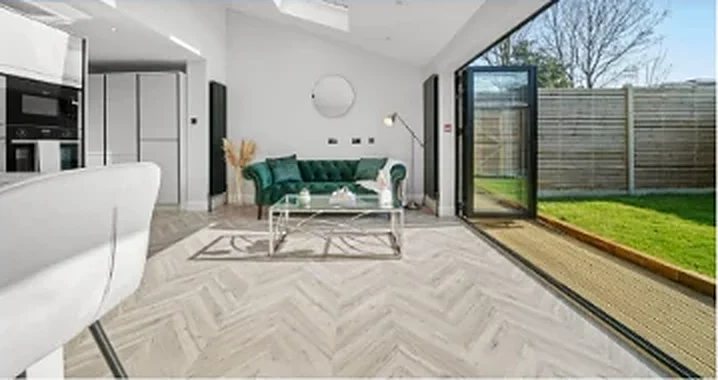 Open-plan living room with a herringbone floor and glazed doors to the garden at Holmesdale Road, London